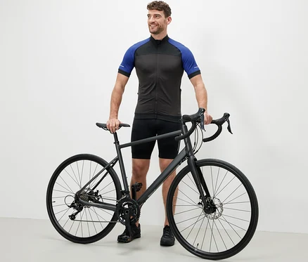 Muž stojí vedle kola v modrém cyklistickém trikotu.