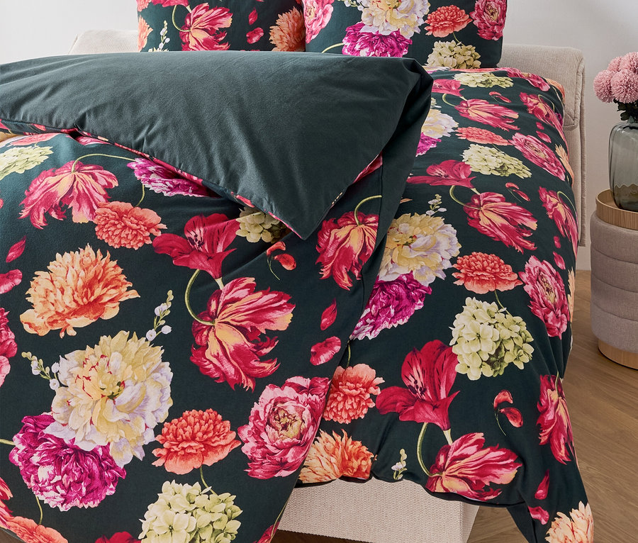 Květinové povlečení na posteli s tmavě zelenou přikrývkou.