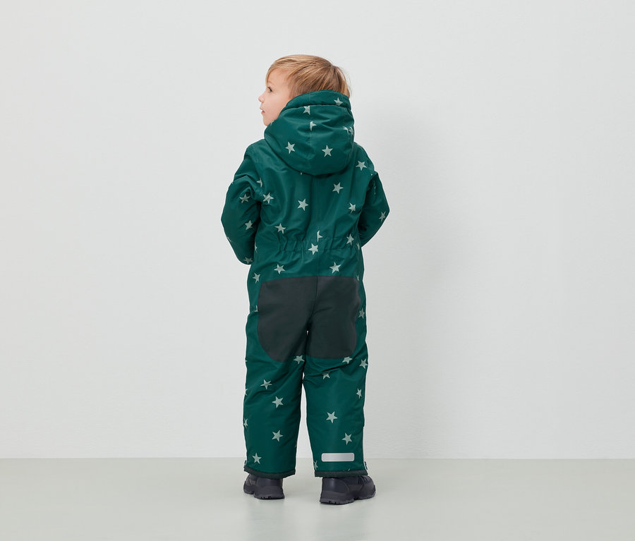 Chlapec v zelené kombinéze se vzorem hvězd stojí zády k fotoaparátu.