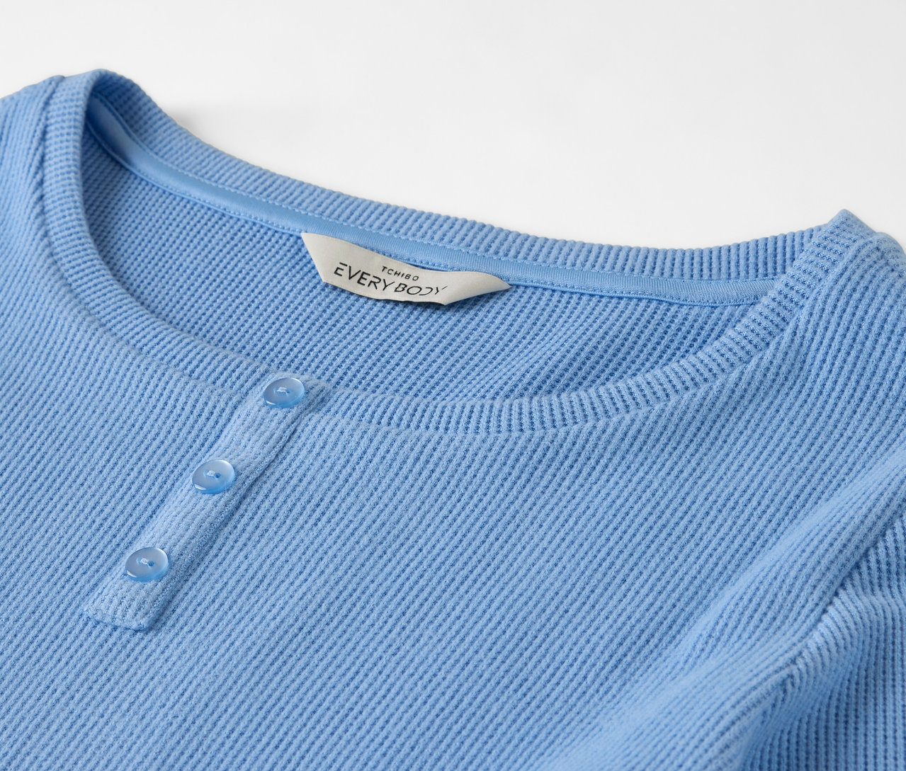 Detail modrého trička s dlouhým rukávem a třemi knoflíčky.