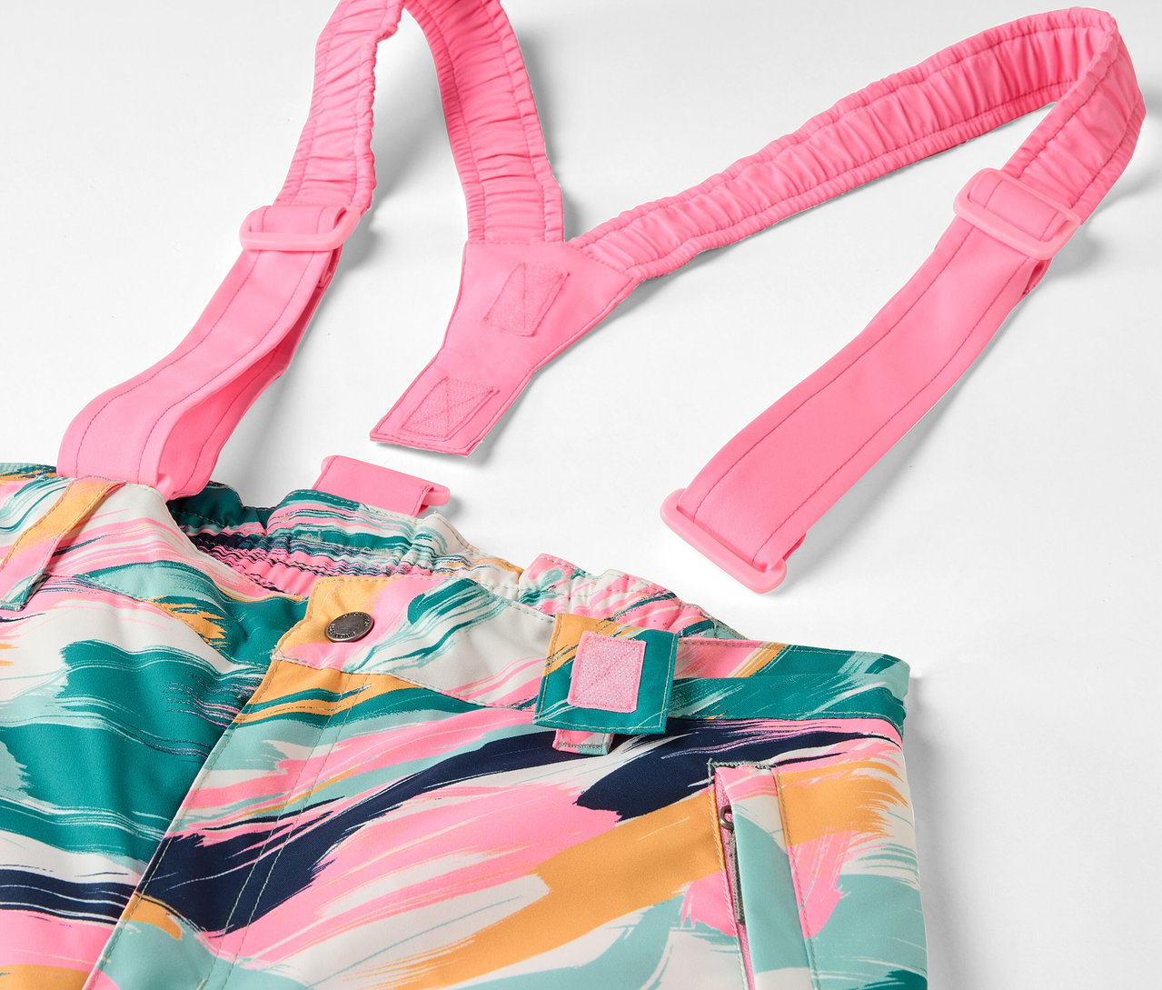 Barevné kalhoty s laclem s abstraktním vzorem a růžovými ramínky.