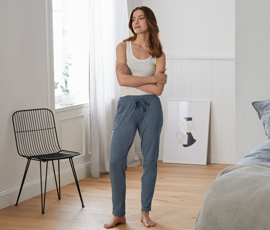 Žena stojí v místnosti a má na sobě pohodlné kalhoty.