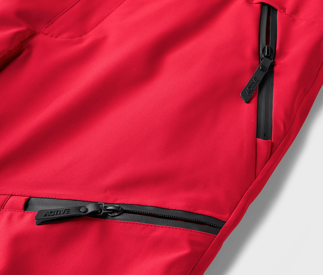 Detail červených kalhot s černými zipy kapes.