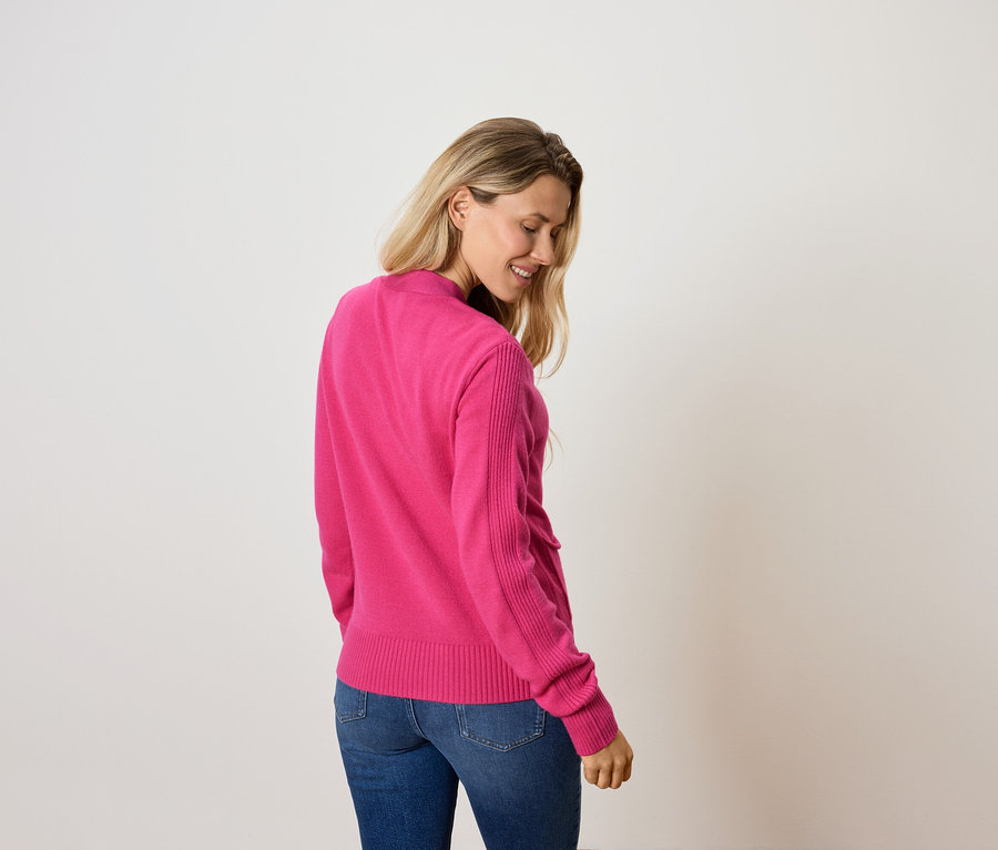 Žena se dívá dolů a má na sobě růžový svetr a džíny.