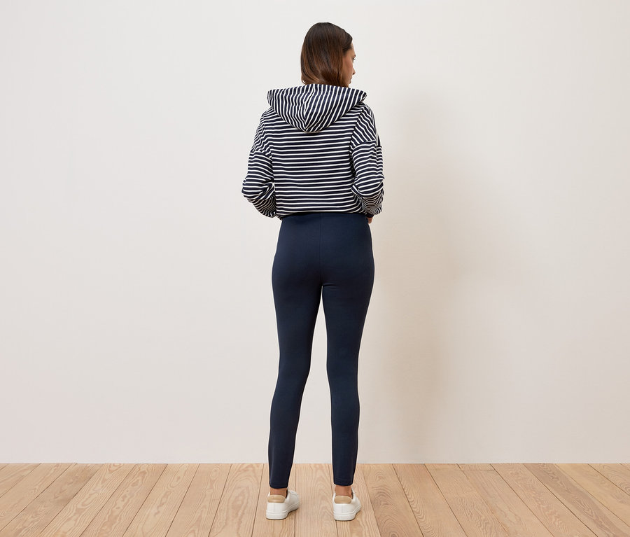 Žena stojí zády k fotoaparátu a má na sobě pruhovanou mikinu s kapucí a tmavě modré legíny.