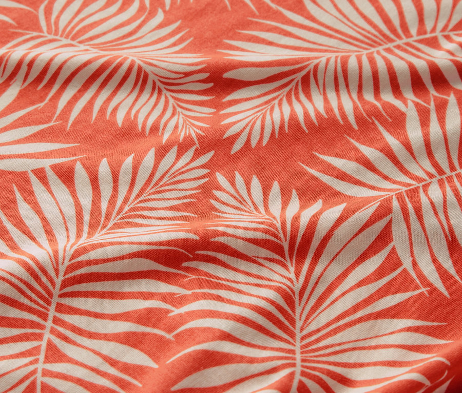 Detailní záběr na halenkové triko s potiskem s motivem bílých palmových listů na korálovém pozadí.