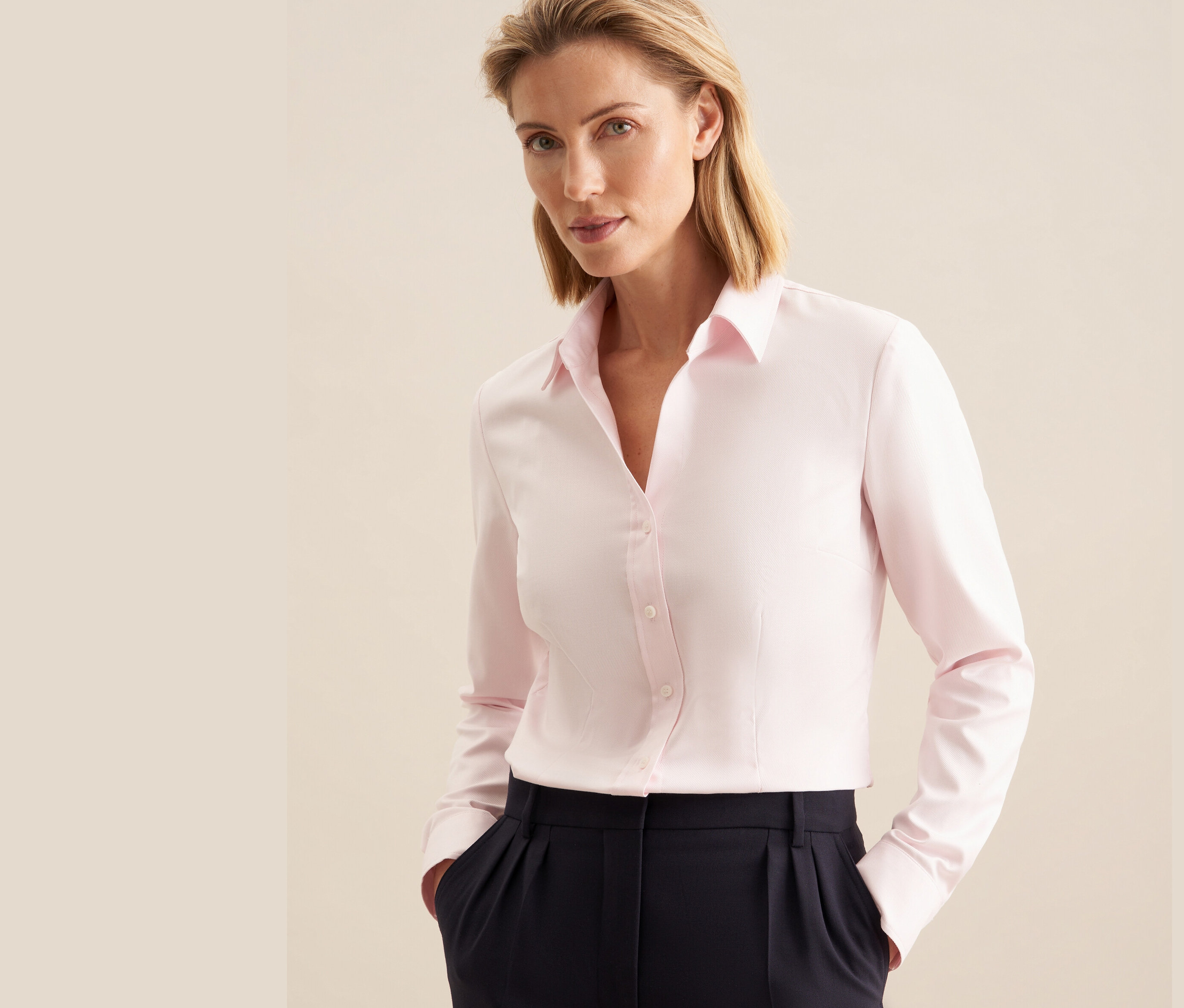 Žena má na sobě světle růžovou keprovou halenku Seidensticker a tmavě modré kalhoty.