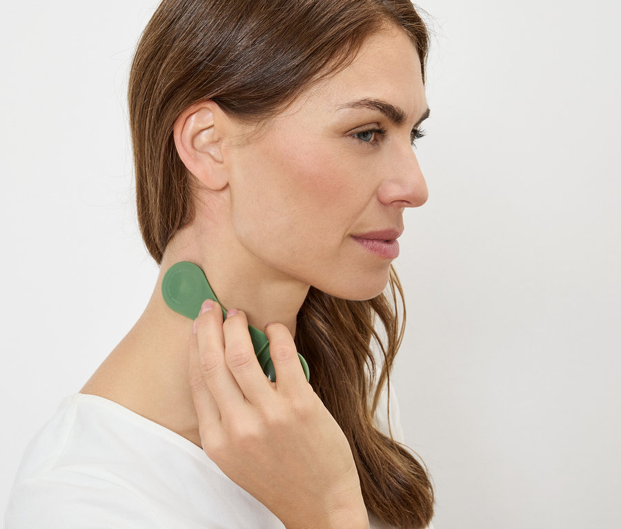Žena masíruje krk zeleným masážním přístrojem.