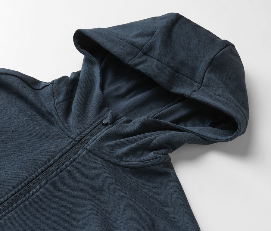 Detail modré mikiny s kapucí na zip na bílém pozadí.