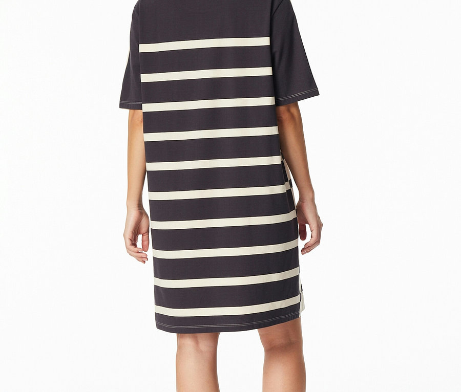 Žena stojí zády k fotoaparátu a má na sobě tmavě šedou noční košili SCHIESSER s krémovými vodorovnými pruhy.