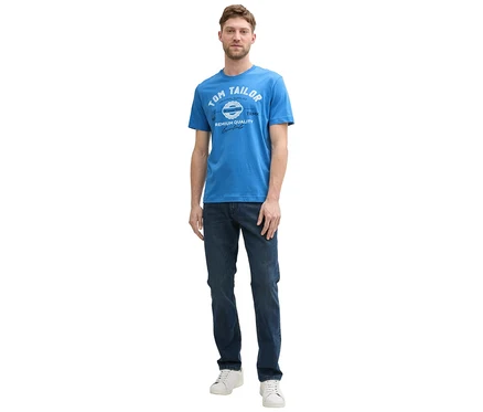 Muž v džínách a bílých teniskách má na sobě tričko s logem Tom Tailor, sapphire blue.