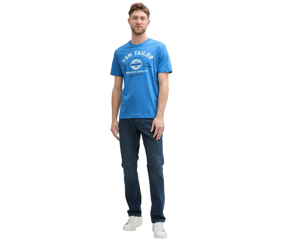 Muž v džínách a bílých teniskách má na sobě tričko s logem Tom Tailor, sapphire blue.