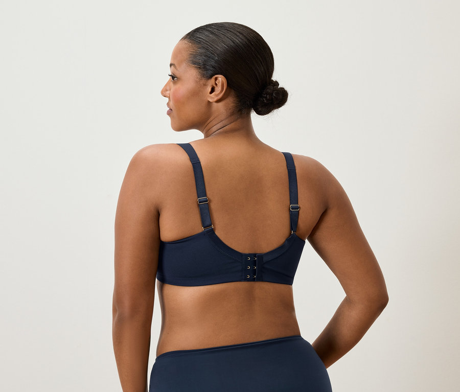 Pohled zezadu na ženu s drdolem, oblečenou v tmavě modré podprsence a kalhotkách.