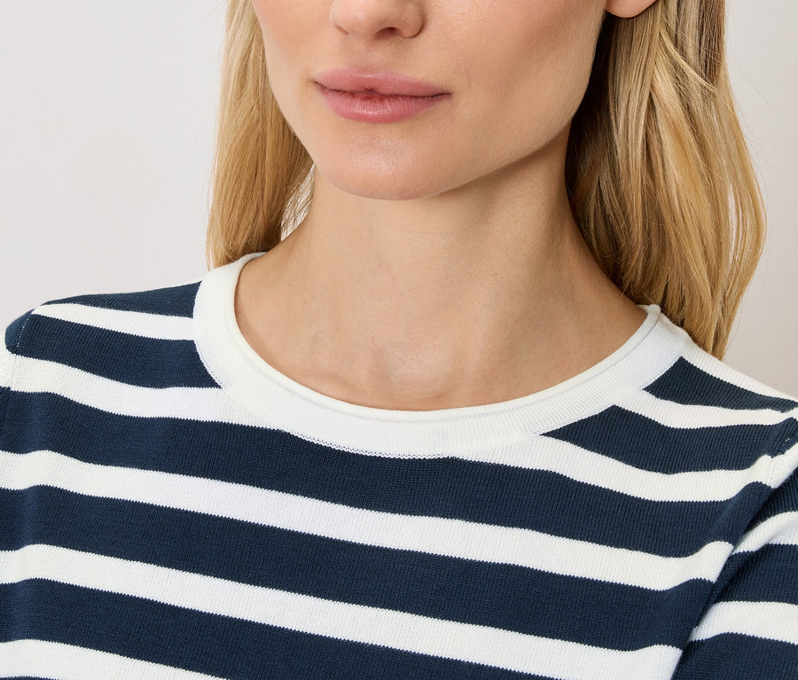 Detailní záběr ženy s blond vlasy v tmavě modro-bílém pruhovaném topu.