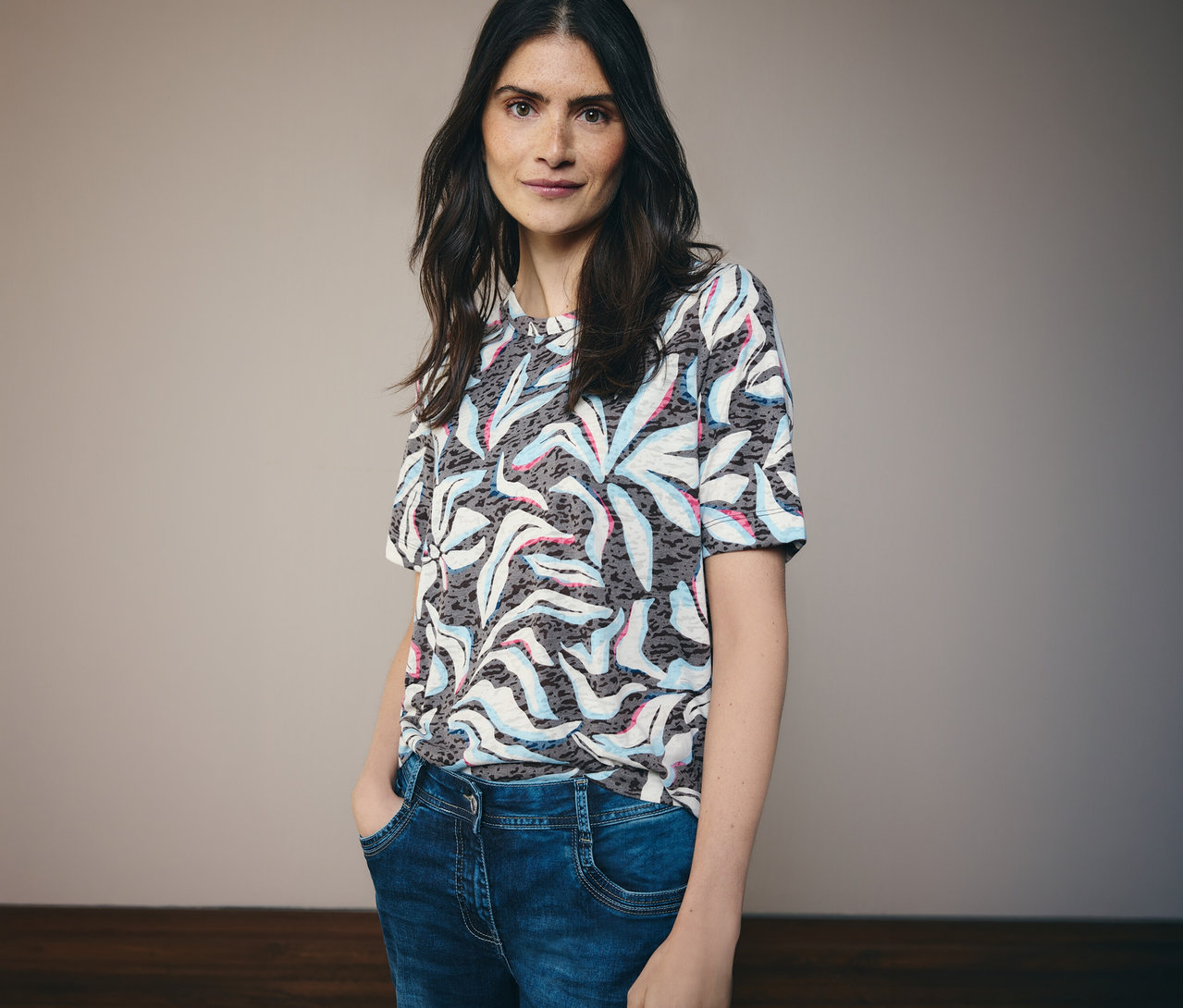 Tmavovlasá žena má na sobě modré tričko s krátkým rukávem CECIL se vzorem a modré džíny.