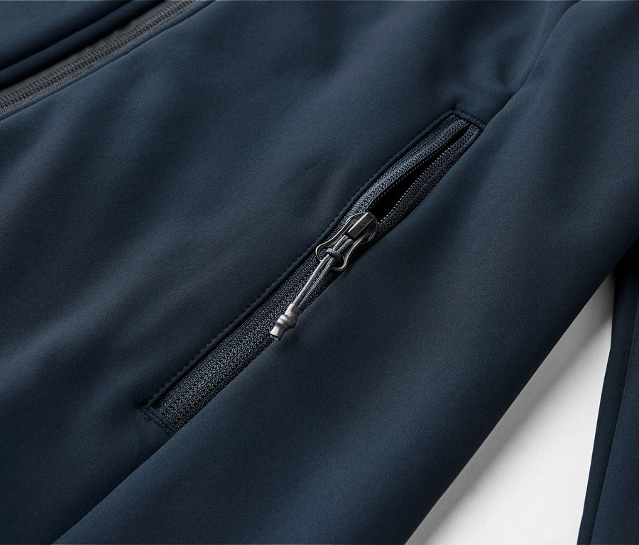 Detailní záběr na tmavě modrou bundu s kapsou na zip a zipem u límce.