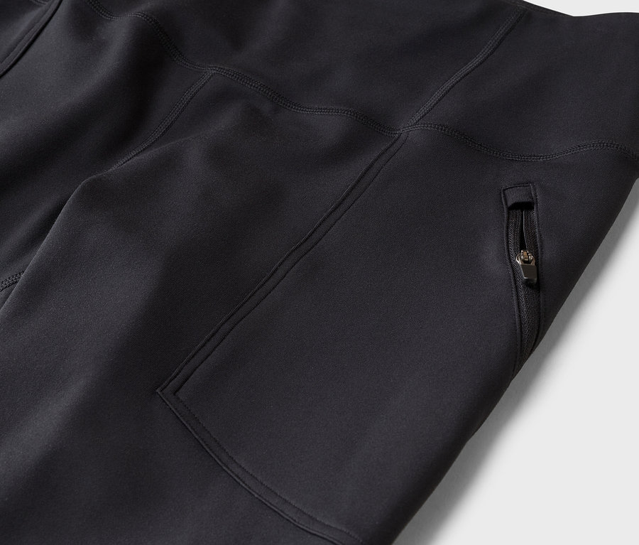 Detail černých sportovních legín nebo kalhot s boční kapsou na zip a viditelnými švy.