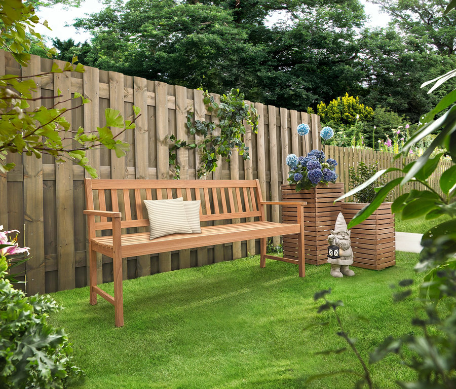 Dřevěná lavička s polštáři stojí na trávníku. Za ní stojí dva květinové sloupy »Tinus« s modrými květinami.