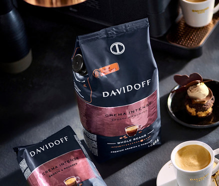Dvě balení kávových zrn Davidoff Crema Intense, šálek kávy a dezert na stole.