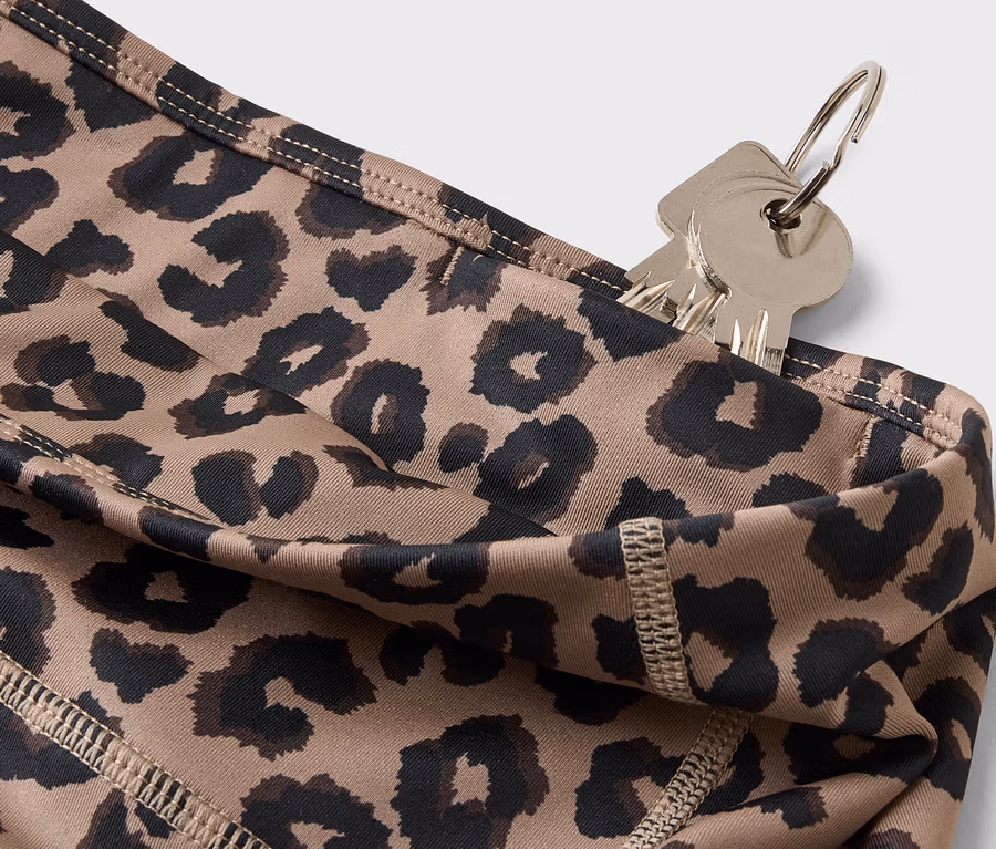 Detailní záběr klíčů zavěšených na kroužku na klíče zasunutých do kapsy legín s leopardím vzorem.