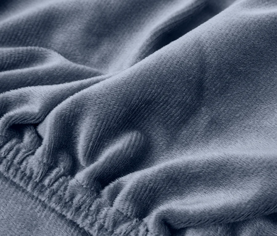 Detail modrošedé plyšové látky s měkkými záhyby a elastickým okrajem.