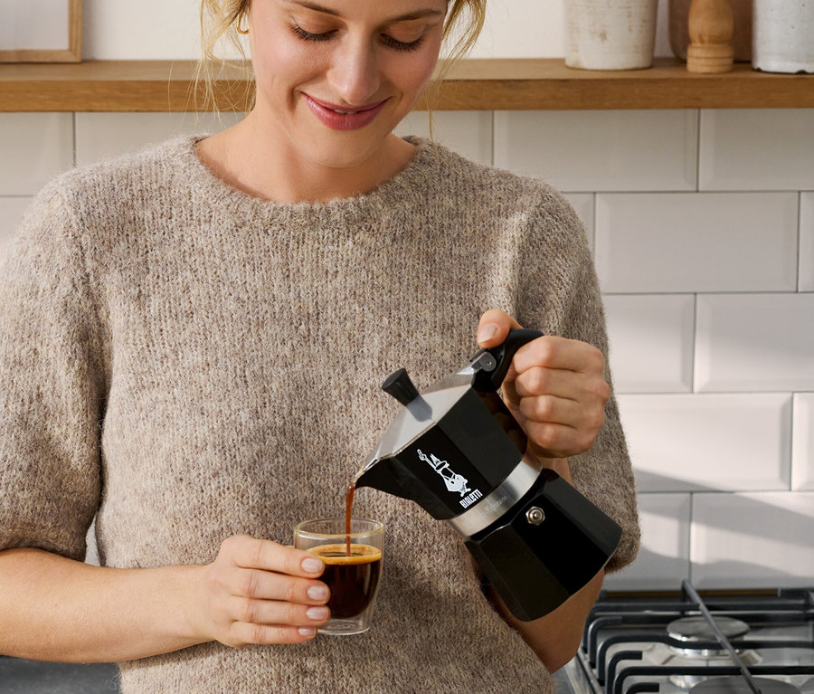 Žena nalévá kávu z černé moka konvice Bialetti Moka Express, 190 ml, do šálku.
