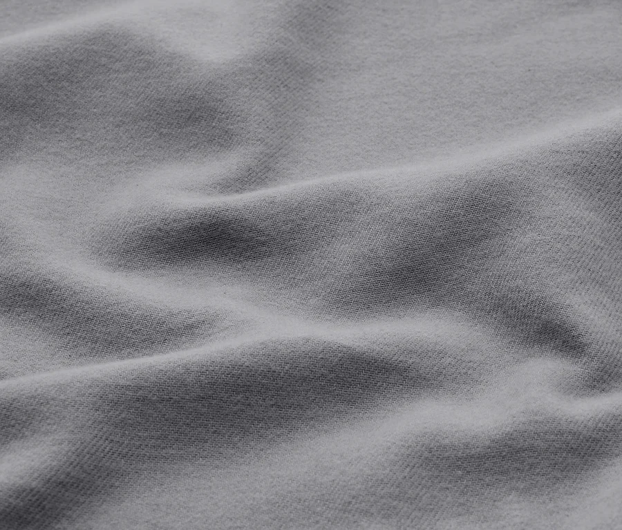 Detail světle šedé, měkké látky s jemnými záhyby a texturou.