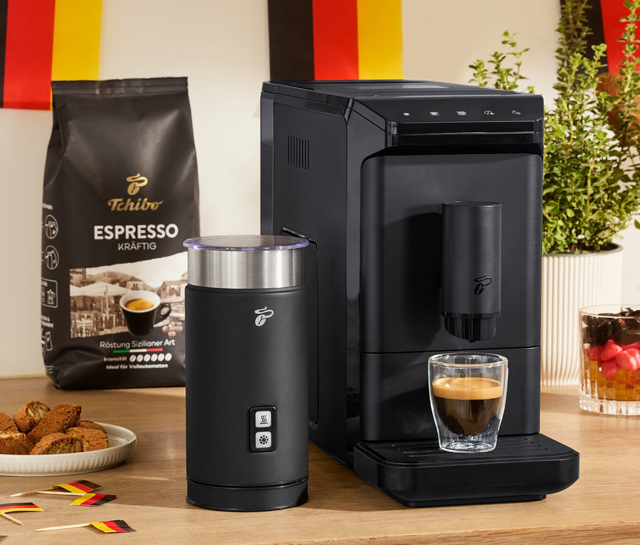 Na stole stojí plnoautomatický kávovar »Esperto mini«, černý elektrický napěňovač mléka a 2 dvoustěnné sklenice na Espresso.