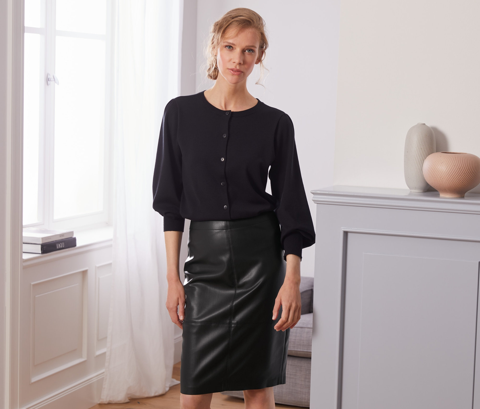 Žena pózuje v černém topu a sukni v koženém vzhledu.