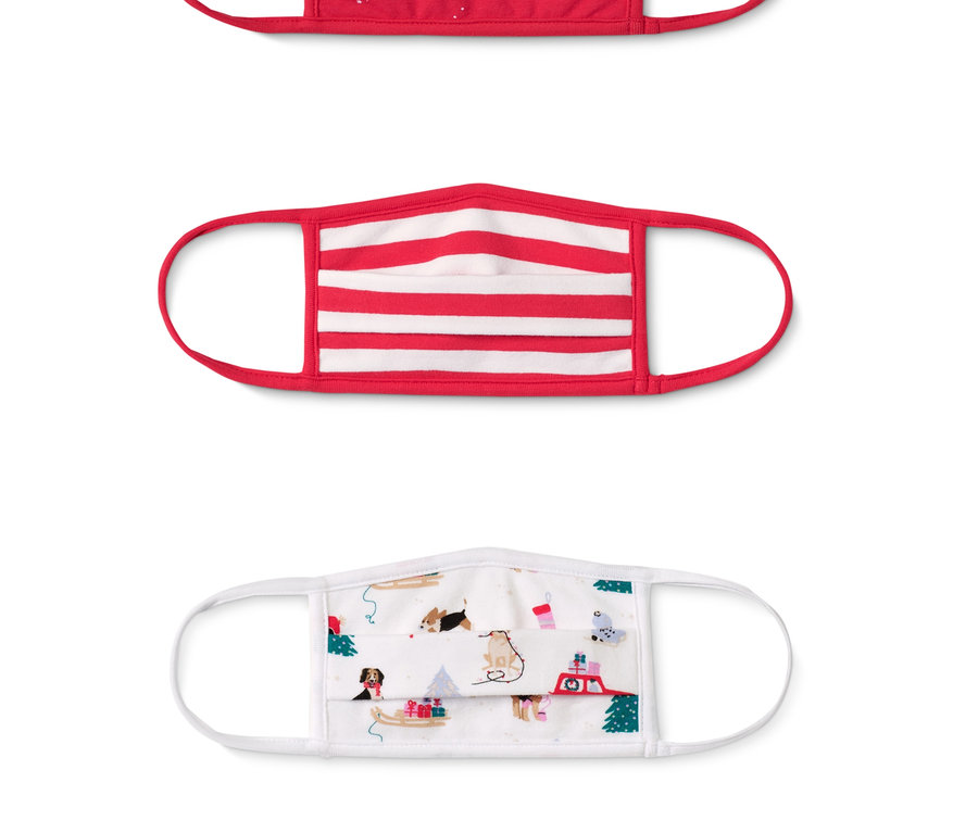 Tři dětské ochranné roušky: červená s vánočními motivy, červenobílá pruhovaná a bílá s potiskem psů a vánočních motivů.