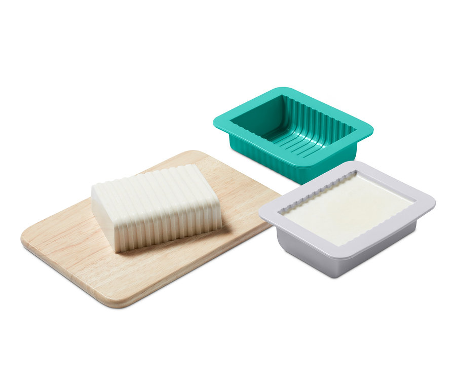 Blok rostlinného másla na dřevěné desce vedle zelené a šedé formy ze sady na výrobu domácího rostlinného másla.