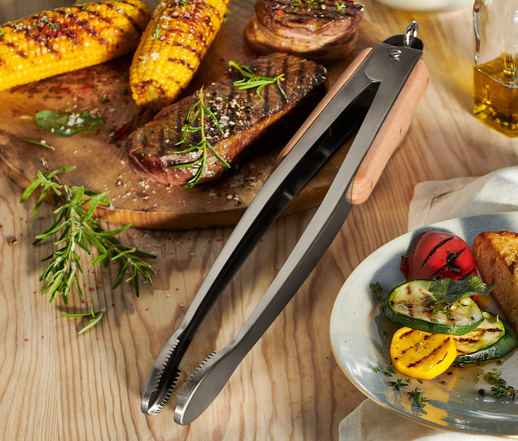 Grilované kukuřice a maso na dřevěném prkénku s grilovacími kleštěmi z ušlechtilé oceli.