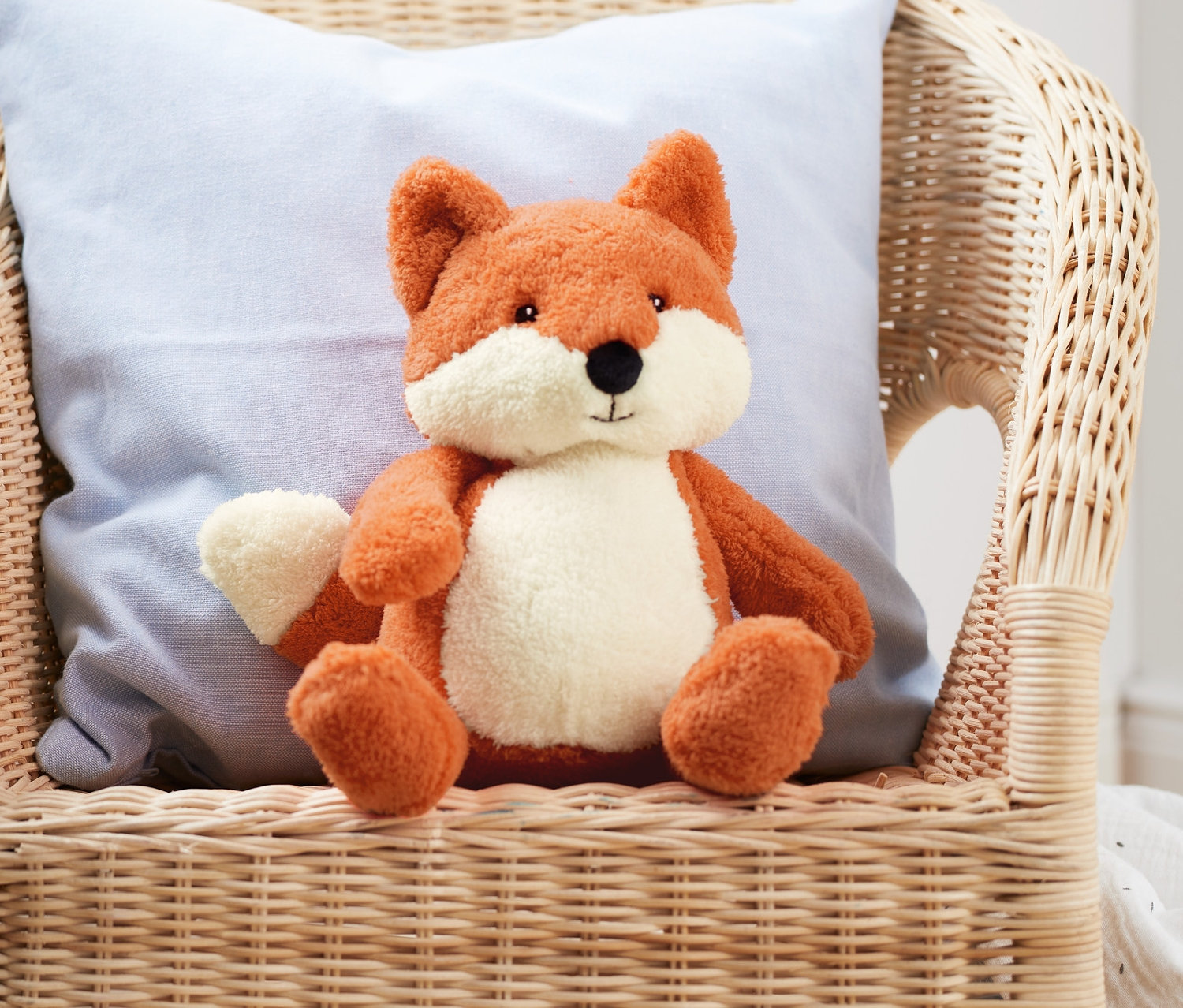 Plyšák Liška sedí na proutěném křesle s modrým polštářem.