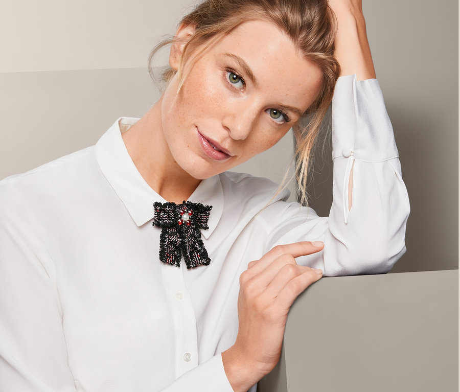 Žena s tvídovou mašlí s broží na bílé košili.