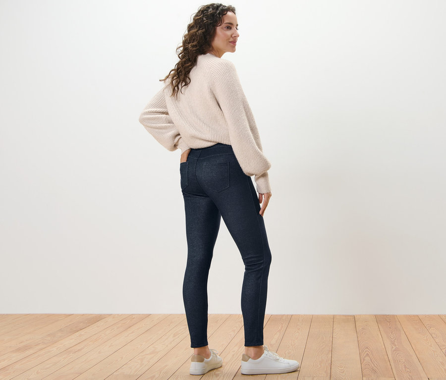 Žena pózuje v džínách s podšívkou a svetru.