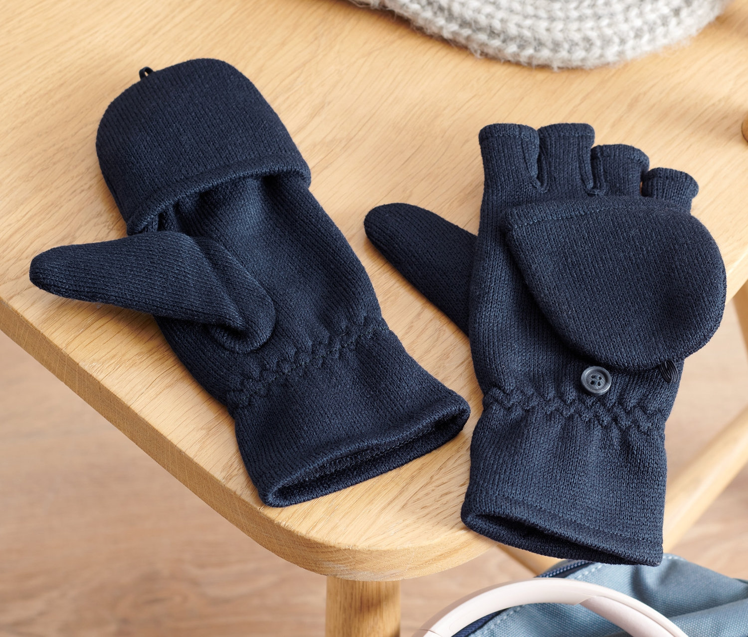 Na dřevěné židli leží dětské odklápěcí rukavice z pleteného fleecu, pletená čepice a sluchátka na batohu.