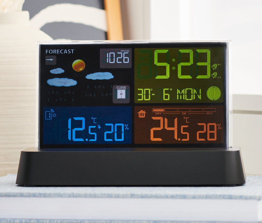 Meteostanice s barevným LC displejem, řízená rádiovým signálem, stojí na knize.