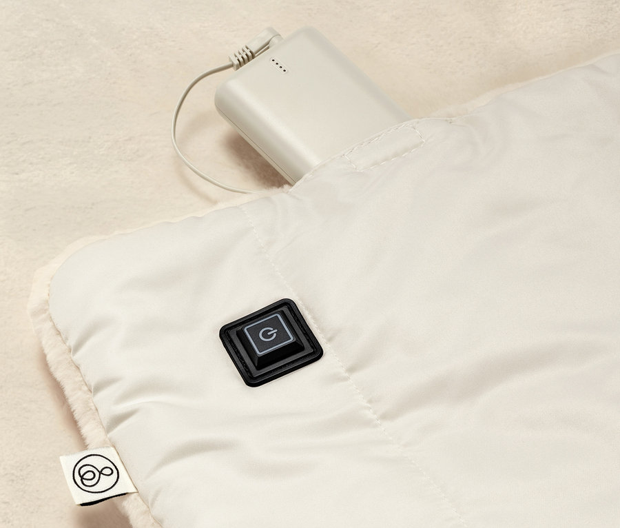 Detailní pohled na vyhřívané pončo na baterie s ovládacím tlačítkem a připojenou baterií.