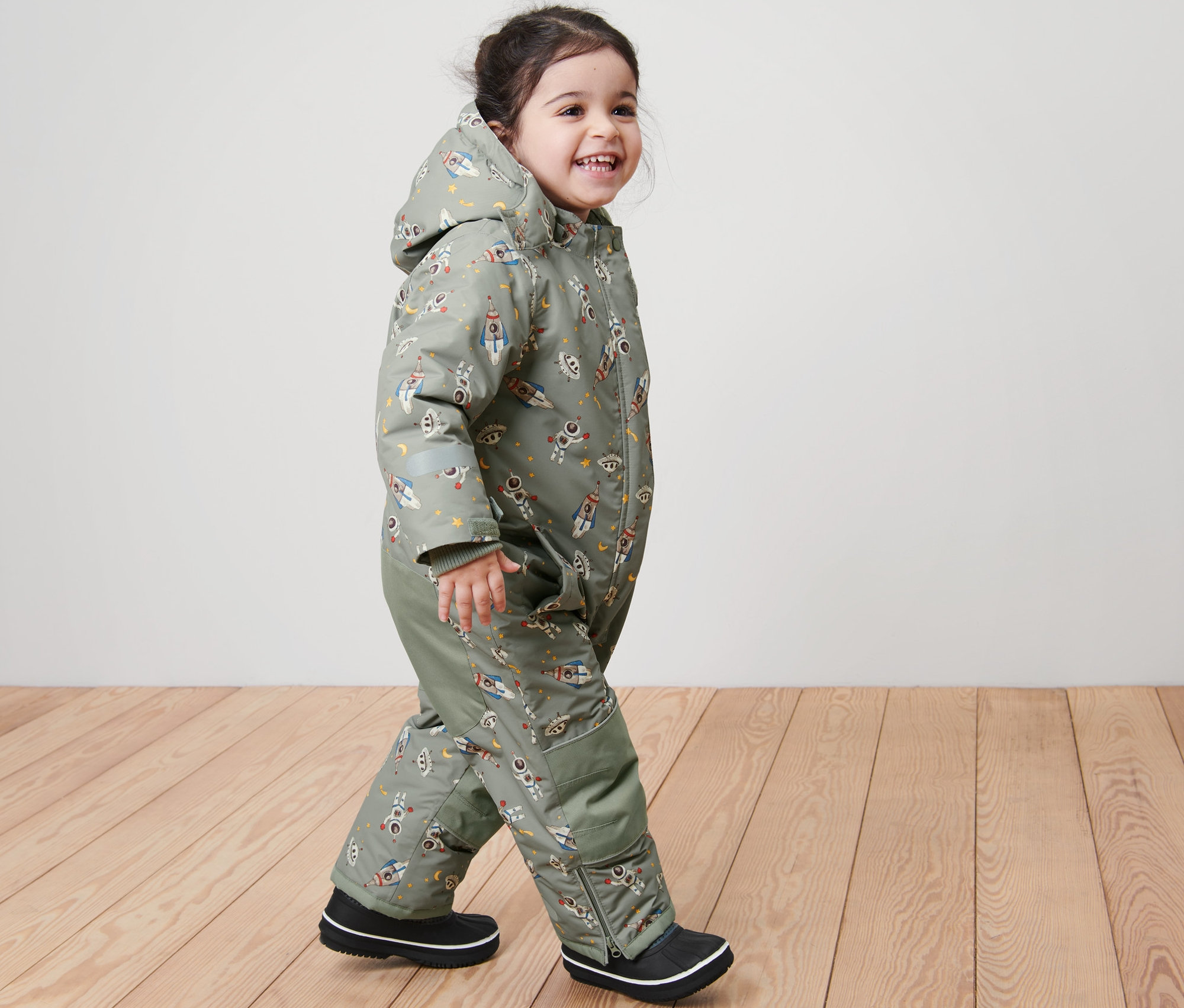 Usmívající se dítě kráčí a má na sobě dětskou zimní kombinézu s potiskem vesmíru.