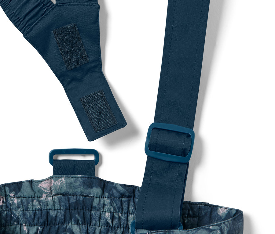 Detail dětských lyžařských kalhot s celoplošným potiskem, včetně nastavovacích popruhů a přezek.