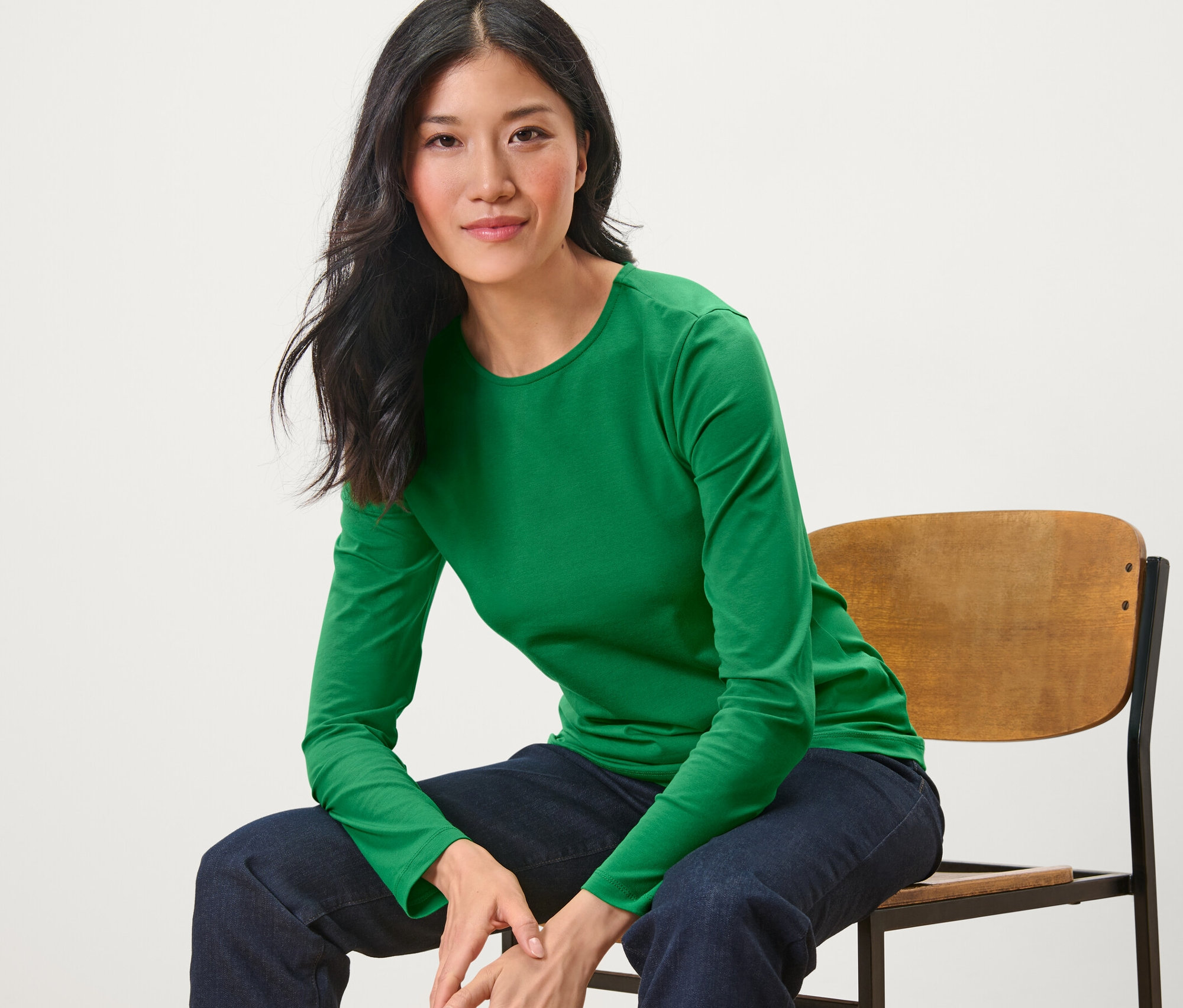 Žena sedí na židli a má na sobě zelené triko s dlouhým rukávem.