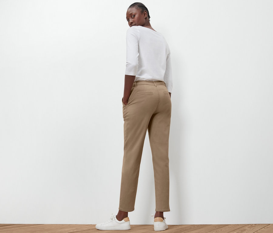 Žena pózuje zády k fotoaparátu a má na sobě béžové kalhoty chino.
