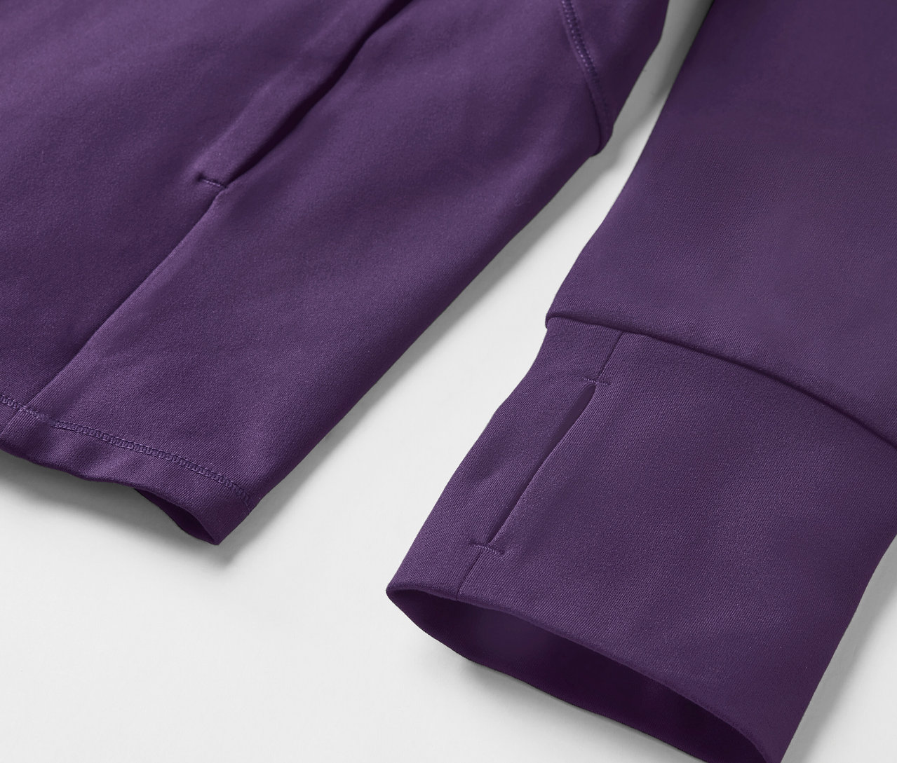 Detail fialové mikiny s dlouhým rukávem s otvory na palce a kapsou na paži.
