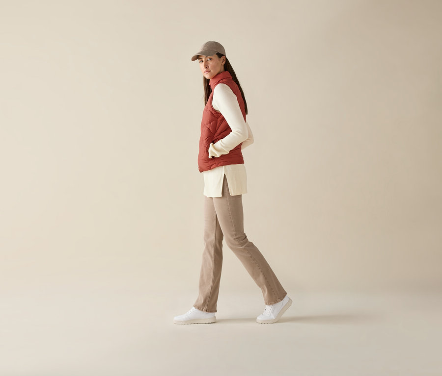 Žena kráčí a má na sobě prošívanou vestu, top s dlouhým rukávem, kalhoty a kšiltovku.