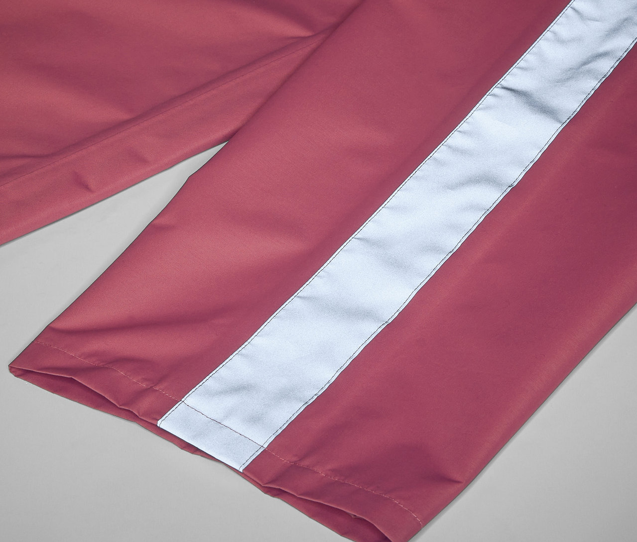 Detail dětských kalhot do deště růžové barvy s reflexním pruhem.