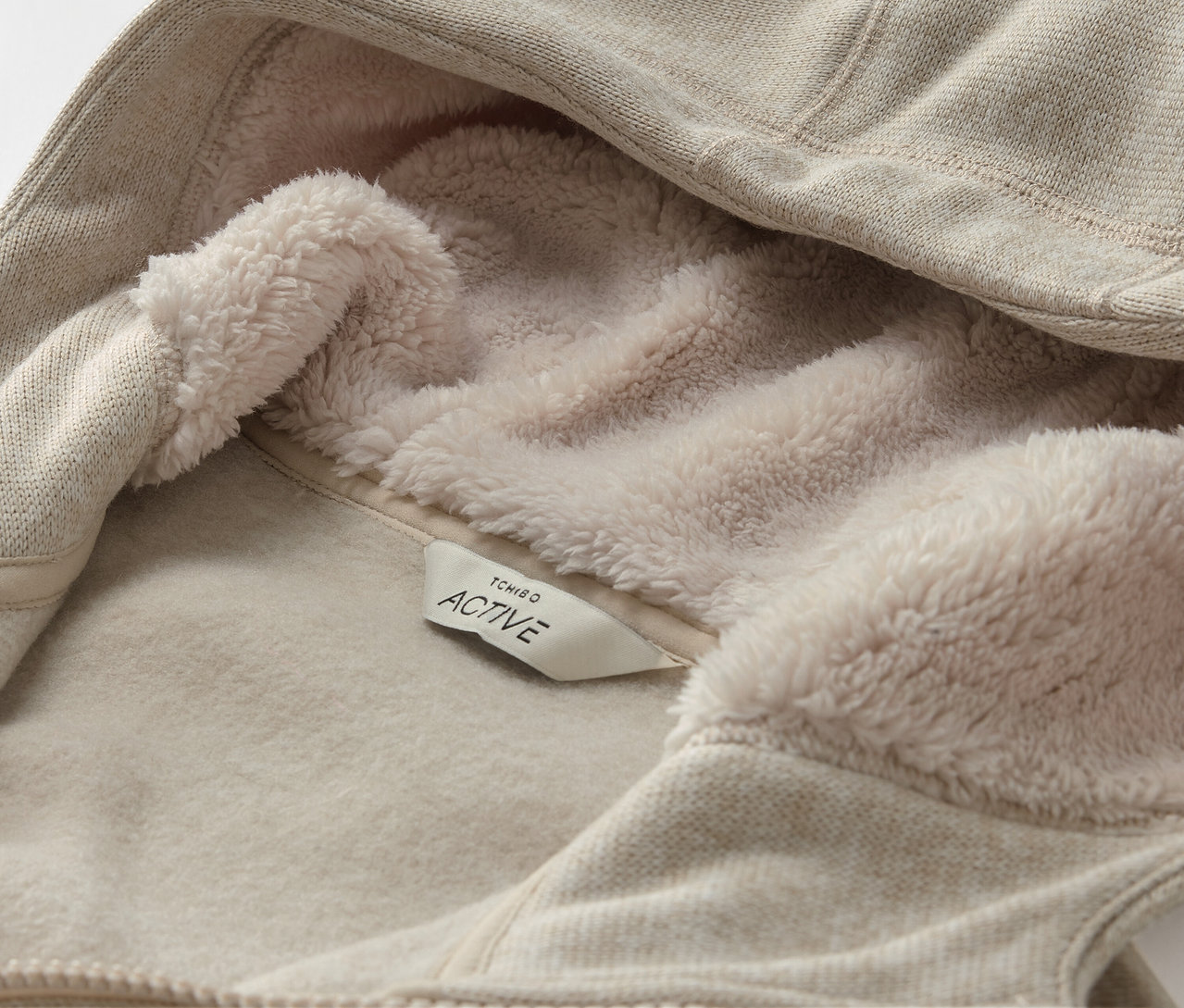 Detail béžové mikiny s kapucí s fleecovou podšívkou a štítkem s nápisem ACTIVE.