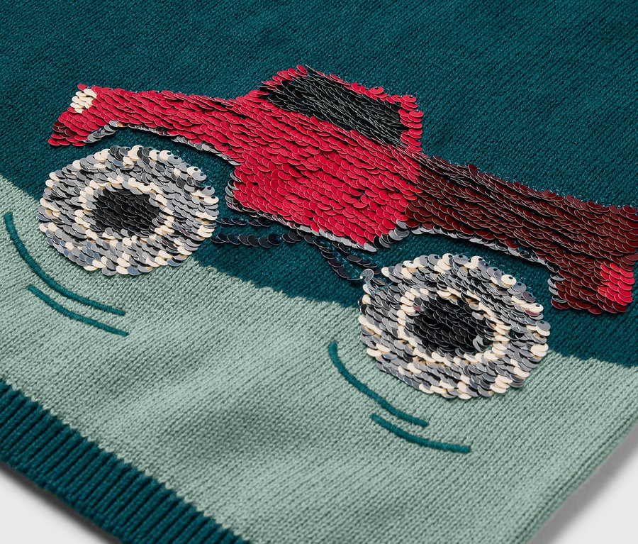 Detail dětského pleteného svetru s nášivkou červeného monster trucku.