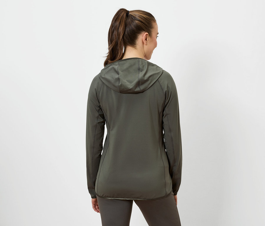 Žena s hnědými vlasy staženými do culíku má na sobě olivově zelenou bundu s kapucí a olivově zelené legíny.