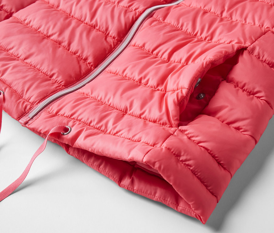 Detail prošívané vesty s kapucí. Vesta je růžová a má stříbrný zip.