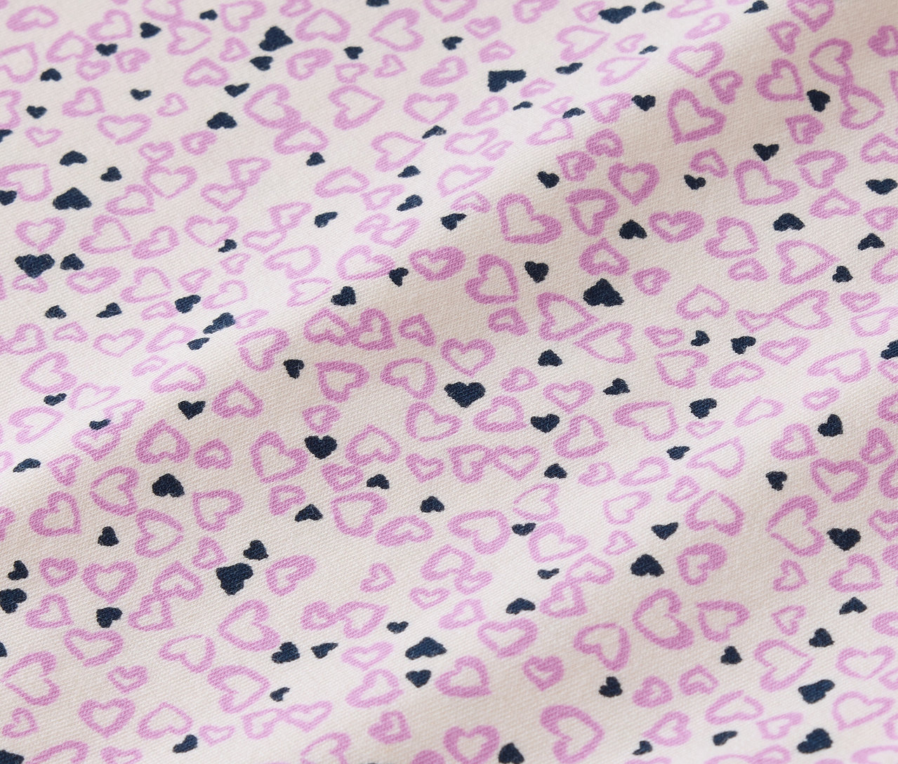Detailní záběr na látku s potiskem malých růžových a tmavě modrých srdíček na bílém pozadí.